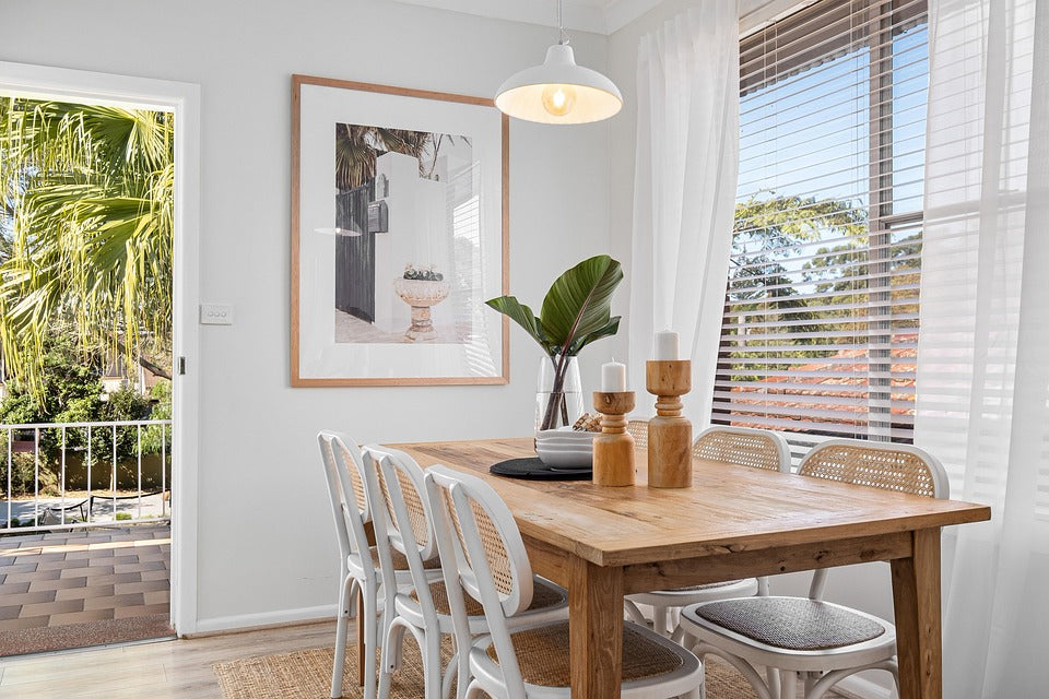 The simple wooden dining table is paired with rattan chairs, and there are unique wooden candlesticks and green plants on the table. The art paintings on the wall echo the white chandelier, presenting a warm restaurant.